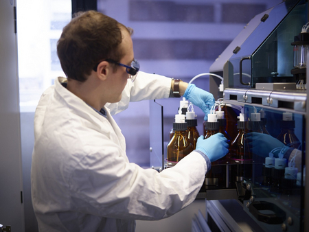 Ein Mitarbeiter in Laborkleidung und Schutzbrillle befüllt Flaschen mit Proben. 